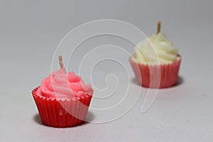 Pink candle in cupcake shape with out focus white candle put on light grey background.