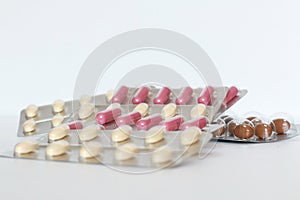 Pink capsules and beige tablets in blisters lie on a white table