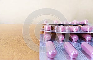 Pink capsules and beige tablets in blisters lie on a white table