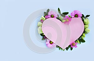 Pink cardboard heart framed with delicate flowers on a light blue background.