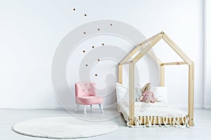 Pink chair against white wall with stickers in simple kid`s bedr