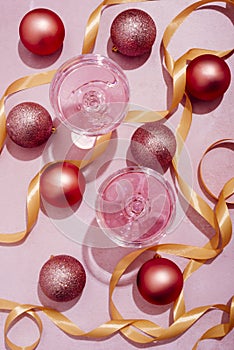 Pink champagne in luxury crystal glasses and christmas baubles with golden ribbon decor. Top view. New year eve celebration and