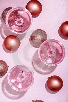 Pink champagne in luxury crystal glasses and christmas baubles with golden ribbon decor. Top view. New year eve celebration and