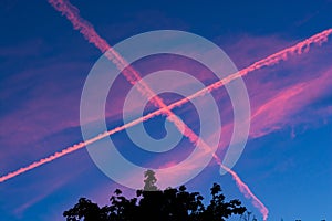 Pink chemtrails on dark blue sky in sunset photo