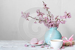 Pink cherry blossom flower bouquet with coffee cup, macaroons and gift box in blue vintage vase