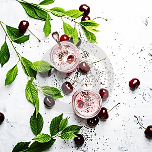 Pink cherry milkshake with berry and chia seeds, white stone background, top view