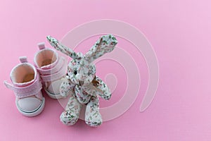 Pink children`s shoes on a delicate pink background. A textile rabbit is sitting nearby. Concept of first steps, birthday,