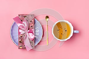 pink chocolate with raisins and nuts on lilac plate, cup of black tea, golden spoon on pink background Dessert Time concept Flat