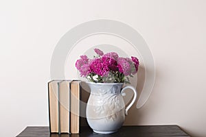 Pink chrysanthemum in a clay rarity vase and books on a wooden table