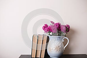 Pink chrysanthemum in a clay rarity vase and books on a wooden table