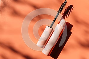 Pink clean makeup brush for mascara lies next to an open tube on a peach background with shadows. Copy space