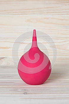 A pink clyster in shape pear with nozzle or tip on wood background. A rubber bulb syringe for douching. Medicine equipment for