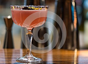 Pink cocktail garnished with flowers in Margarita glass