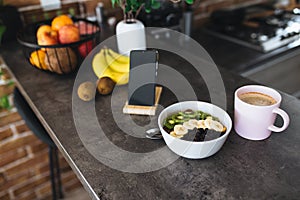 Pink coffee cup, chopped fruits in bowl and blueberries, spoon, phone in kitchen