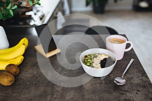 Pink coffee cup, chopped fruits in bowl and blueberries, spoon, phone in kitchen