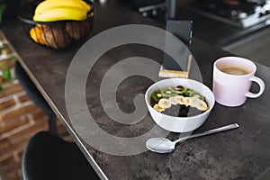 Pink coffee cup, chopped fruits in bowl and blueberries, spoon, phone in kitchen