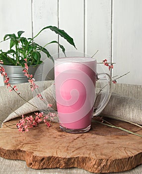 Pink coffee latte macchiato in a glass cup on a wooden backing decorated with dried flower