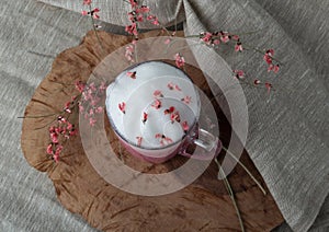 Pink coffee latte macchiato in a glass cup on a wooden backing decorated with dried flower