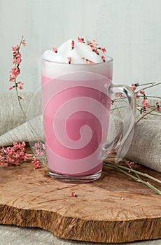 Pink coffee latte macchiato in a glass cup on a wooden backing decorated with dried flower