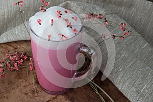 Pink coffee latte macchiato in a glass cup on a wooden backing decorated with dried flower