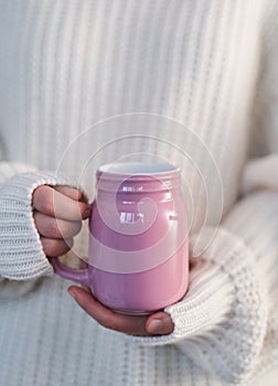Pink coffee mug in female hands with white sweater