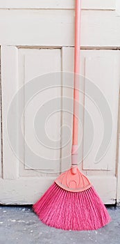 Pink colour fan broom in a standing position along with  off whitedoor