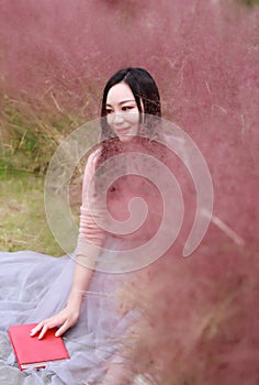 Pretty beautiful cute Asian Chinese woman girl reading book in a flower field outdoor in summer autumn fall park grass lawn garden