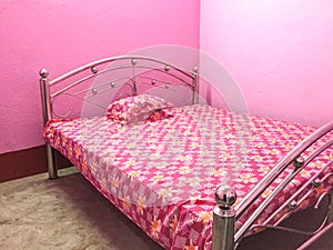 Pink coloured bed with floral bed sheet with pink walls