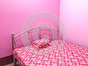 Pink coloured bed with floral bed sheet with pink walls