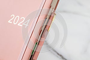 Pink coral colored diary for the year 2024, pen, marble background