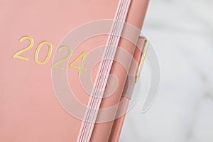 Pink coral colored diary for the year 2024, pen, marble background