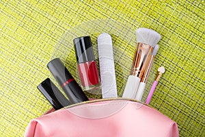 Pink cosmetic bag and decorative cosmetics for a makeup of a young woman on a green background