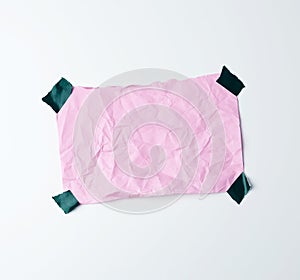 Pink crumpled sheet of paper glued with adhesive tape on a white background