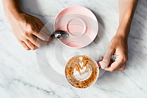 Pink cup of fresh cappuccino in woman hands on white marble table background