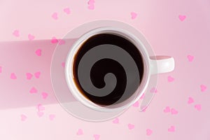 Pink cup with hot black tea on pink background with scattered paper hearts. Love and care concept