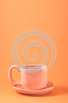 pink cup with a saucer on a orange background/pink cup of coffee on a orange background, close up