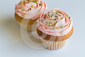 Pink cupcakes on white background - frosted cup cakes decorated with green pistachio sprinkles - with selective focus