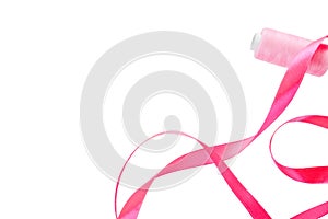 Pink curly satin ribbon and a spool of pink thread on a white background. Horizontal banner, on the left side a satin ribbon and