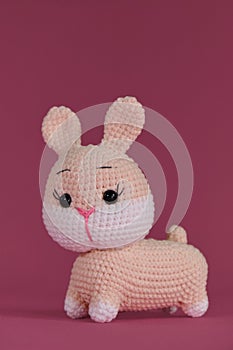 Pink cute Easter bunny crocheted, handmade art. Amigurumi rabbit doll on pink background. Soft DIY toy made of cotton