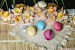 Pink daffodils and biscuits on burlap with painted Easter eggs lie on straw carpet