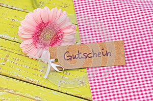 Pink daisy flower and gift tag with german word Gutschein, means voucher or coupon for mothers or valentines day