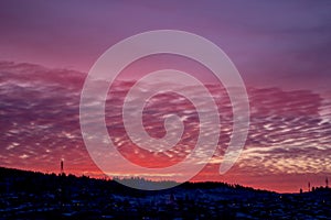 Pink dawn over a small town. City silhouette with a beautiful sunset. Dark winter landscape, outlines of mountain and forest