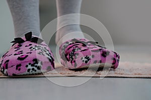 Pink domestic slipper for women with black bow stand on the floor on a light plush rug, concept of comfortable shoes for rest,