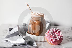 Pink donut with marshmallow and hot chocolate in glass cup on marble table.