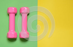 Pink dumbbells isolated on green yellow background with copy space. Womens fitness equipment