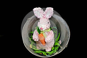 Pink Easter bunny made out of flower petals with yard carrot in a bucket -flowers on black background