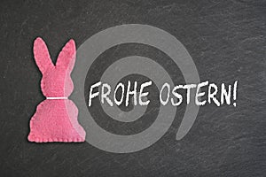 Pink Easter bunny with text `Frohe Ostern` on a chalkboard background. Transla