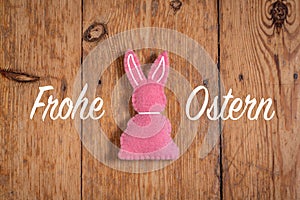 Pink Easter bunny with text `Frohe Ostern` and a wooden background. Translation: `Happy Easter`