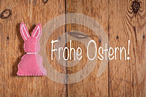 Pink Easter bunny with text `Frohe Ostern` and a wooden background. Translation: `Happy Easter`