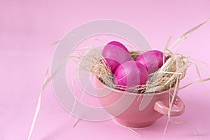 Pink Easter eggs in a pink plate with straw on a pink background